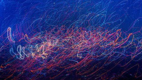 Swirling neon light trails forming dense multicolor band over deep blue night sky