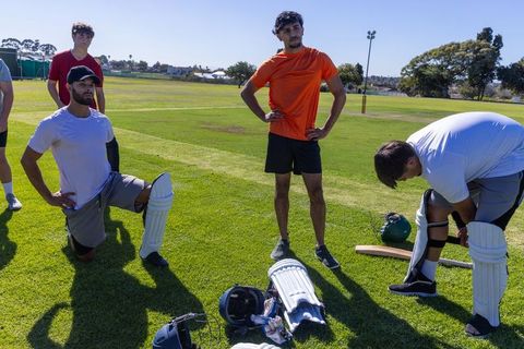 Diverse cricket team preparing batting gear for practice on sunny outdoor field