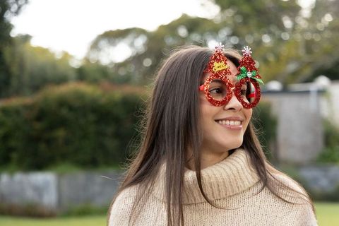 Smiling young woman wearing red glitter christmas tree glasses in backyard garden