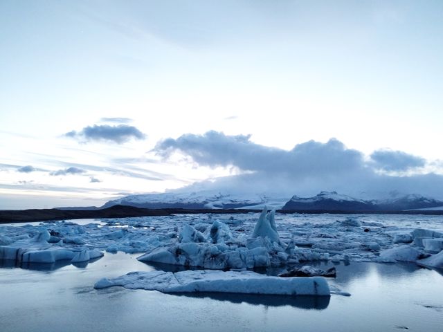 Pristine glacier lagoon with floating icebergs during dusk. Serene water and distant snowy mountains offer a tranquil natural scene. Ideal for travel articles, nature blogs, environmental awareness campaigns, and backgrounds for outdoor enthusiasts.