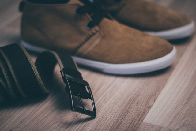 Closeup of casual brown shoes placed on a wooden floor with a belt lying nearby. Useful for articles or content about men's fashion, casual style, accessories, lifestyle blogs, or promotional materials for footwear brands.