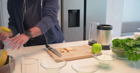 Diverse men preparing banana spinach smoothie on kitchen counter with blender and yogurt