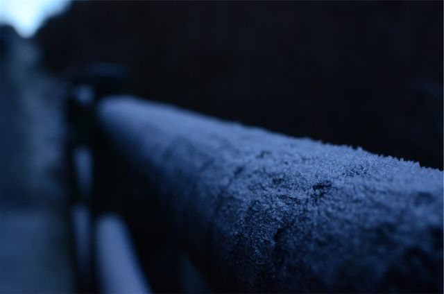 Close-up view of frost-covered metal railing during early morning, capturing the cold and moody atmosphere of winter. Perfect for use in winter weather blogs, promotional materials for seasonal clothing, or decorative prints in home or office settings.