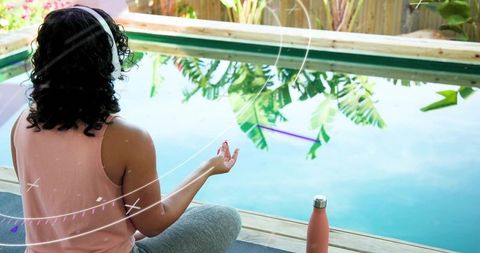 Woman meditating poolside wearing headphones during backyard yoga and mindfulness practice