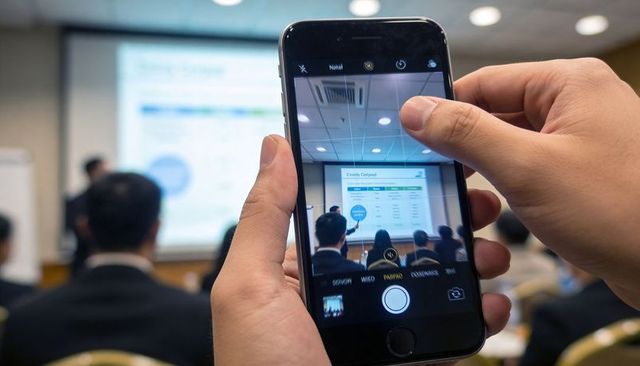 Capturing presentation on smartphone at business conference with slide charts and audience