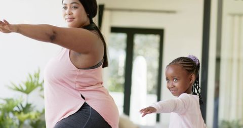 African american mother and daughter practicing yoga and stretching in sunlit living room