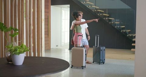 Young couple entering minimalist hotel lobby pointing toward staircase with luggage