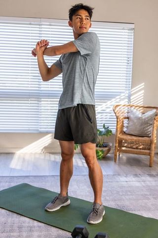 Asian man stretching on exercise mat in bright minimalist living room during home workout