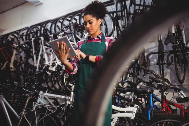 Image depicts a female bicycle mechanic using a digital tablet while working in a bike workshop. Ideal for promoting technology integration in traditional trades, advertisements for bike shops or repair services, and illustrating the modern workplace.