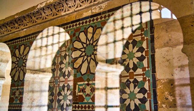 Ornate geometric mosaic panel inside carved stone arch casting window grid shadows