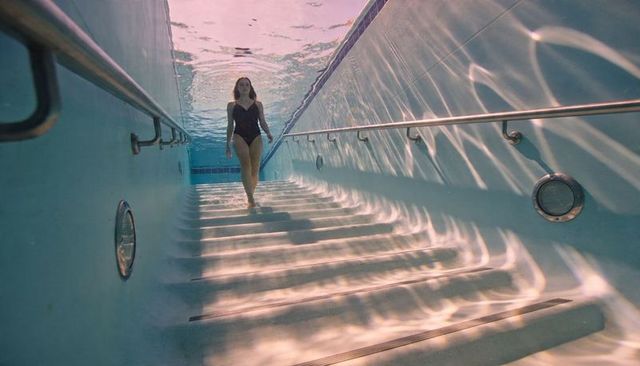 Underwater woman walking down pool steps with handrails and shimmering light caustics