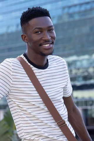 Smiling african american man in striped tee with crossbody bag in urban plaza