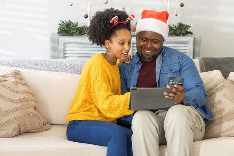 African american father and teen daughter sharing tablet for holiday shopping on couch