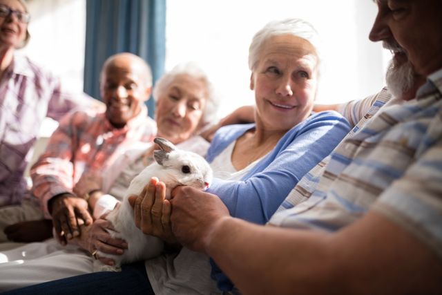 Senior woman holding rabbit while sitting with friends on sofa at nursing home
