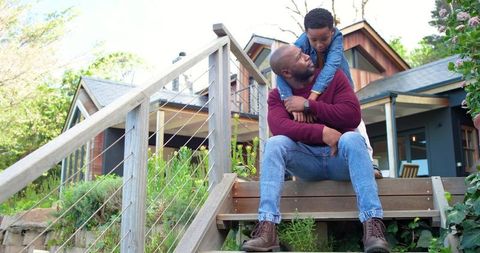 African american father and son embracing on craftsman porch steps during sunny day