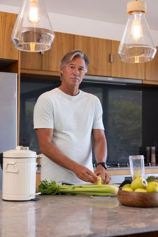 Middle-aged man preparing celery and peeling fruit on modern kitchen island