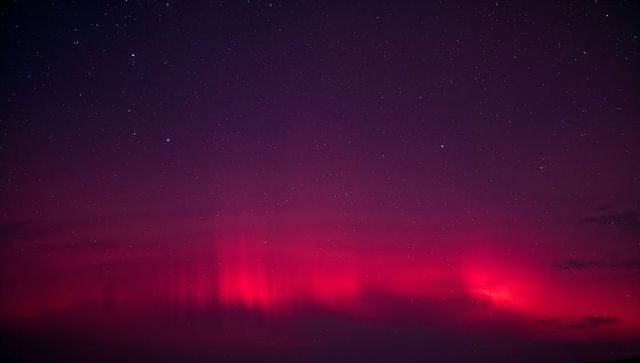 Glowing magenta aurora dancing over starry night horizon