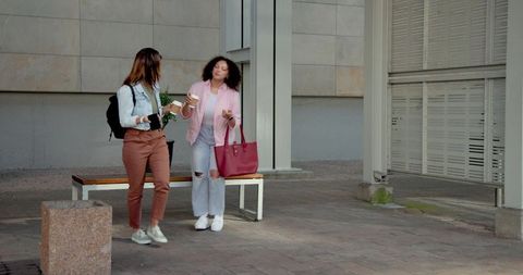 Diverse women walking and chatting with takeaway coffee and smartphone in urban plaza