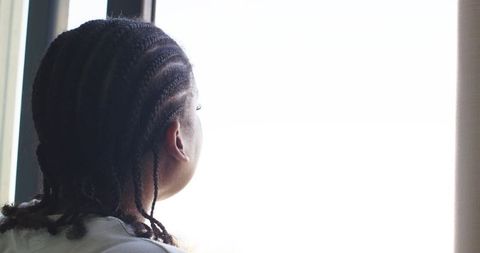 African american woman with cornrow braids contemplating at bright window backview calm
