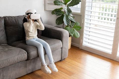 Young girl experiencing virtual reality headset on gray couch in sunlit living room