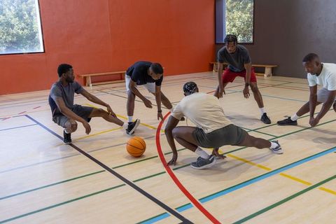 African american men stretching together on indoor basketball court before workout