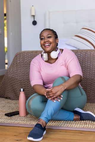 Smiling african american woman relaxing in activewear with headphones and water bottle