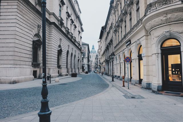 Scenic view of a tranquil, historic European street lined with classical buildings. The cobblestone and ornate details of the architecture make it a charming sight. Ideal for use in travel blogs, architectural studies, cultural explorations, and promotional material for tourism.