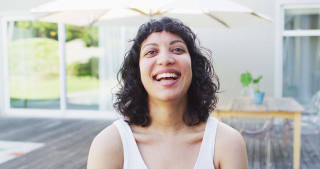 Portrait of laughing biracial woman outside on terrace of modern house in the sun. domestic lifestyle, spending free time at home.