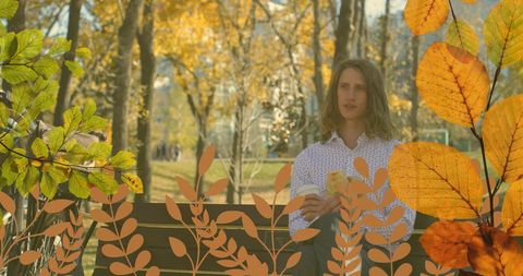 Man Enjoying Coffee on Park Bench Amidst Golden Autumn Foliage