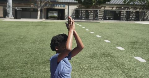 Young african american athlete raising arms in celebration on football turf