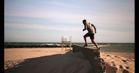 Athletic Young Man Running on Beach and Jumping Over a Wall