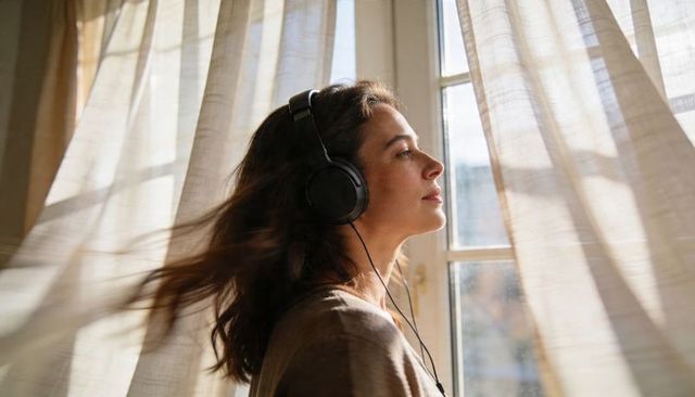 Woman listening to music by sunlit window with flowing sheer curtains