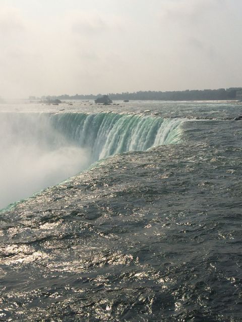 Niagara Falls showing powerful waterfall cascading into river below with mist rising. Ideal for travel promotions, nature blogs, tourism and geography education.