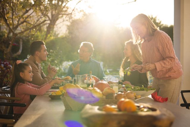 Caucasian senior woman serving food to multi-generation family talking while having lunch in yard. Unaltered, love, together, meal, childhood, sunlight, copy space, winter, dining table and lifestyle.