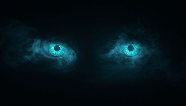 Glowing turquoise eyes in mysterious darkness