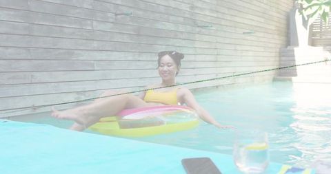 Woman relaxing on colorful inflatable ring in private pool with smartphone and lemon drink