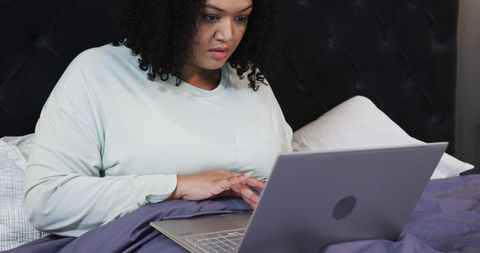 Mid-adult African American woman working on laptop in cozy bedroom, remote work and study