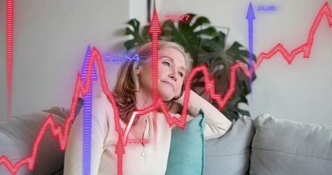 Pensive woman gazing at market charts while relaxing on sofa with home plants and cushions