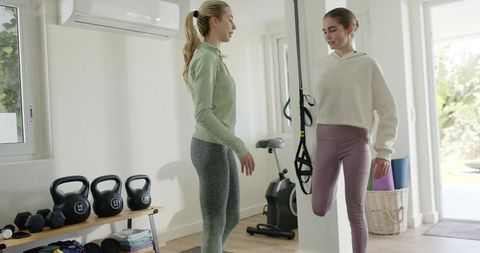 Female trainer guiding balance with suspension straps in bright home gym workout