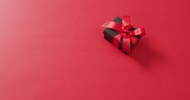 Black gift box with red ribbon on red background with copy space. Luxury treat, present, shopping, black friday sale and retail concept digitally generated image.