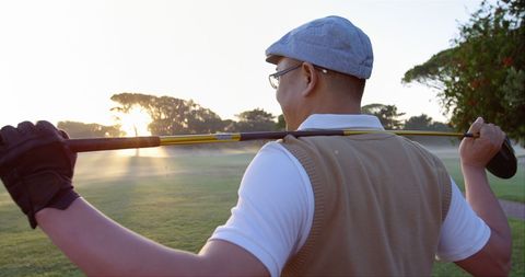 Golfer is smiling while carrying a golf club over shoulders on a scenic golf course during sunrise. This image captures the relaxed and joyful atmosphere of a morning spent golfing. Ideal for use in promotions related to sports, leisure activities, retirement lifestyles, or outdoor hobbies.