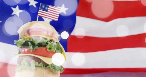 Stacked cheeseburger with american flag toothpick, usa flag bokeh background, patriotic bbq