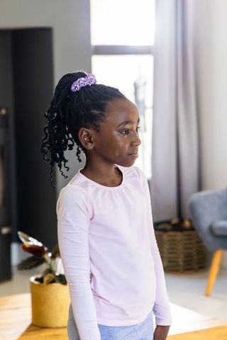 African american girl standing looking right in sunlit home wearing pink top purple scrunchie