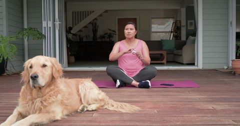 Asian woman practicing mindfulness on wooden deck patio with golden retriever companion