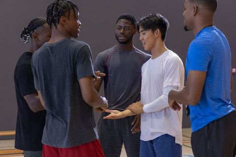 Diverse male teammates discussing strategy and teamwork on indoor basketball court