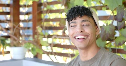 Sunlit african american man smiling on patio wearing beanie and olive tee, candid portrait