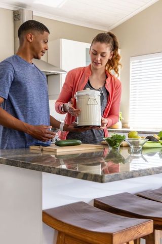 Couple cooking at kitchen island inspecting compost pail for sustainable meal prep