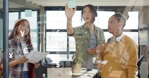 Three women collaborating on glass board, brainstorming sticky notes and financial ideas
