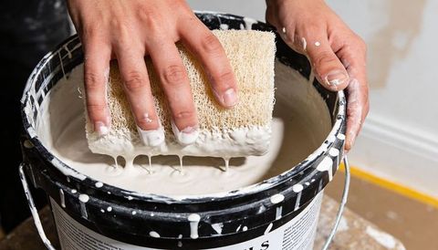 Painter dipping loofah sponge into white primer bucket hands covered in paint diy