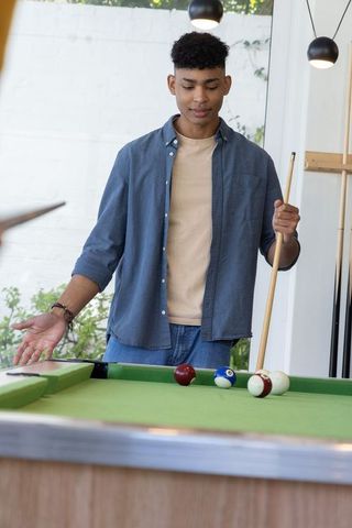 African american teen playing pool in modern game room under pendant lights